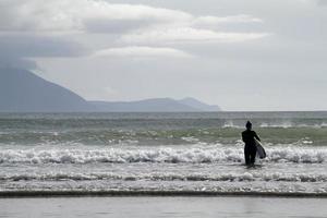 Beach near Dingle, Ireland - July 10, 2019 - Surfer in the sea at the coast near Dingle, Ireland, with mountains in the background. photo