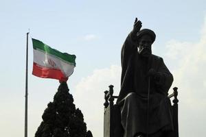 Tehran, Iran - June 10, 2018 - A large Iranian flag waving in the wind behind a statue of Khomeini in Tehran, Iran photo