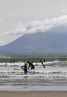 Beach near Dingle, Ireland - July 10, 2019 - Surfers diving into the sea at the coast near Dingle, Ireland, with mountains in the background. photo