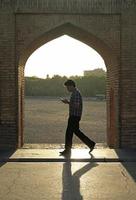 Isfahan, Iran - June 14, 2018 - A man walks on the famous Khaju Bridge in the evening hours while checking his smartphone. photo