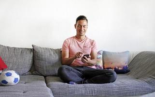 hombre sonriente manejando smartphone mientras está sentado en el sofá foto