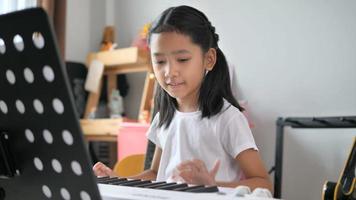 Asian little girl learning to play basic piano by using electric synthesizer keyboard for beginner music instrumental self studying at home video