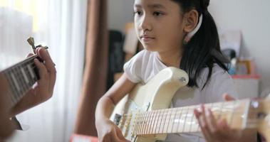 Asian little girl learning to play basic guitar by using electric guitar for beginner music instrumental self studying at home video