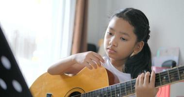 padre enseñando a una niña asiática aprendiendo a tocar guitarra básica usando guitarra eléctrica para principiantes de música instrumental autoestudio en casa