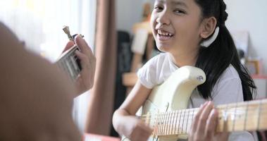 Asian little girl learning to play basic guitar by using electric guitar for beginner music instrumental self studying at home video