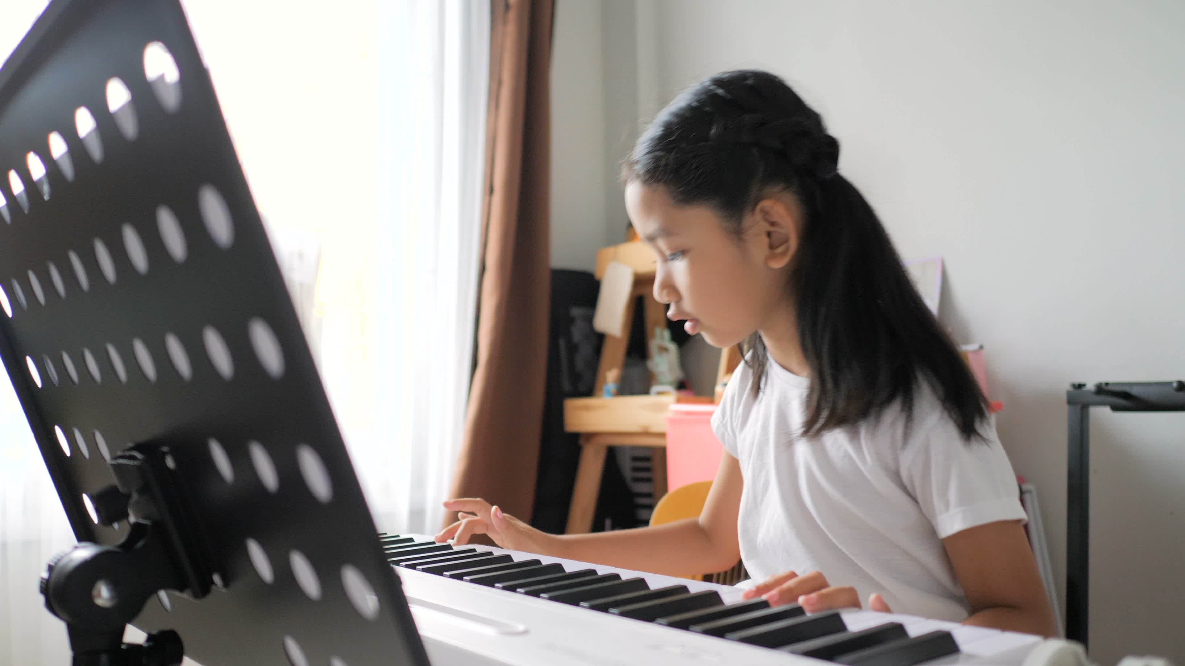 Criança asiática aprendendo a tocar piano online em casa