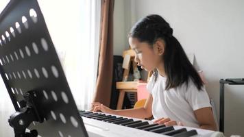 Asian little girl learning to play basic piano by using electric synthesizer keyboard for beginner music instrumental self studying at home video