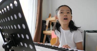 Asian little girl learning to play basic piano by using electric synthesizer keyboard for beginner music instrumental self studying at home video