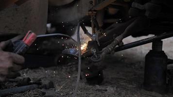 Hands of mechanic welding for repair the truck wishbone control arm of front wheel with dark and grain processed