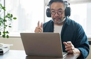 hombre asiático de mediana edad sentado en casa trabajando en una videollamada. trabajo desde el concepto de casa foto