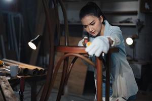 La joven carpintera asiática de diseñador de muebles usa una cinta métrica para medir la silla en el banco de trabajo en el taller de carpintería de madera.