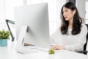 Young asian girl working at a home with a computer and wearing earphones photo