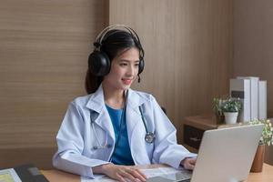 Asian Female doctor wear headphones  video call consultation, patient and doctor talk concept. photo