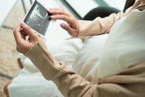 Asian pregnant woman looking at ultrasound picture at home photo