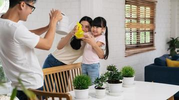 familia asiática regando las flores de las plantas y jugando juntos en casa foto