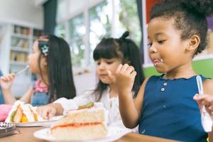 cute little child girl with friends eating cake together. photo