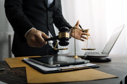 Justice and law concept.Male judge in a courtroom with the gavel, working with, computer and docking keyboard, eyeglasses, on table in morning light photo
