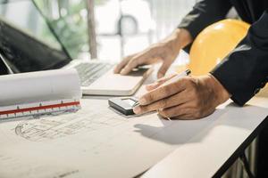 Dos colegas discutiendo el trabajo de datos y una tableta, un portátil con un proyecto arquitectónico en el sitio de construcción en un escritorio en la oficina foto