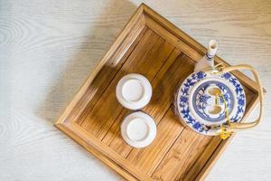 top of traditional white cup of tea and teapot in wooden tray closeup on table