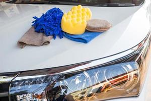 Yellow, green sponges and blue mitts for washing and microfiber fabric with cleaner cloth on white car