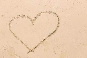 corazón dibujado en la suave arena de la playa. concepto de amor foto