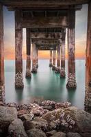 Dark of underneath the pylons of a long jetty pier beach overlooking the sea at sunset or twilight at Khao Laem Ya Mu Ko Samet National Park Rayong, Thailand. Seascape long exposure shot photo