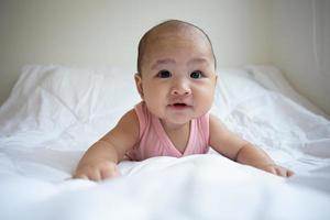 Asian cute baby in white sunny bedroom. Newborn child relaxing on bed photo