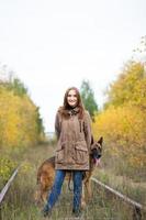 Linda mujer joven con perro pastor alemán posando en el bosque de otoño cerca de la vía férrea foto