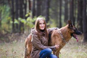 Young attractive woman posing with German Shepherd dog and smiling outdoors in the autumn park, close up photo