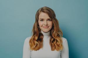 Beautiful dreamy young woman with perfect wavy styled hair in white turtleneck smiling at camera photo