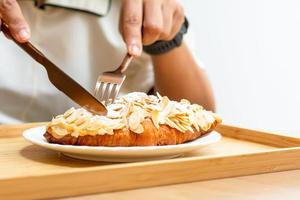 Desert and sweet bakery concept. Eating croissant almonds with a knife and frok on a white plate in cafe and coffee shops. photo