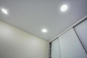 halogen spots lamps on suspended ceiling and drywall construction in in empty room in apartment or house. Stretch ceiling white and complex shape. photo