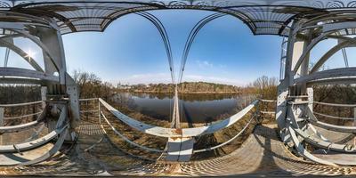 panorama hdri esférico completo sin costuras vista de 360 grados de ángulo en la torre del puente de madera de suspensión peatonal sobre el río ancho en un día soleado en proyección equirectangular. skybox para contenido vr ar foto