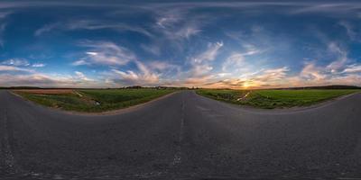 Full spherical seamless panorama 360 degrees angle view on old no traffic asphalt road among fields in evening  before sunset with cloudy sky in equirectangular projection, VR AR content photo