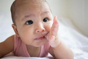 Asian cute baby in white sunny bedroom. Newborn child relaxing on bed photo