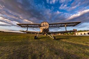 viejo avión destruido en el campo en los rayos del sol poniente con hermosas nubes foto