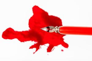 top view of steel nib in dip pen over red ink blot photo