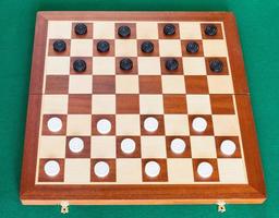 draughts on wooden board on green table photo