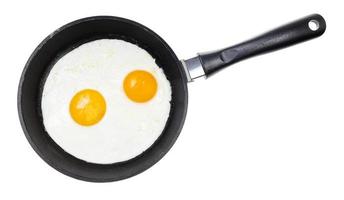 top view of two fried eggs in black pan isolated photo