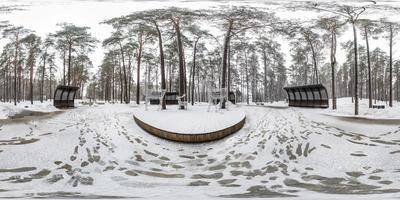 Winter full spherical seamless hdri panorama 360 degrees angle view on pedestrian road in snowy park with gray pale sky near arches and benches in equirectangular projection. VR AR content photo