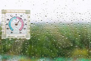 gotas de lluvia y termómetro húmedo en el cristal de la ventana foto