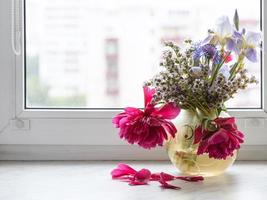 various flowers in glass vase on window sill photo