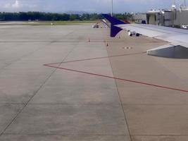 Airplane wing with docked ladder at the airport field apron, taxiway with red line marking photo