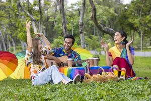 grupo de jóvenes amigos lgbtq de diversidad haciendo un picnic en el jardín mientras disfrutan cantando música en el parque público al aire libre durante el verano con alegría y felicidad foto