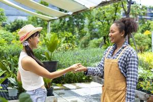 Asian customer is having handshake with African owner of exotic plant in the local garden center nursery duringummer plant for weekend gardening and outdoor pursuit photo