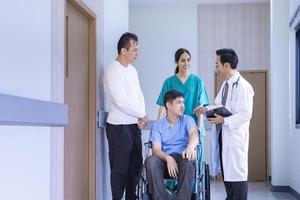 Team of doctor from is discussing with the nurse and parent about kid patient in wheelchair at his appointment in hospital for physical therapy after knee surgery from accident photo