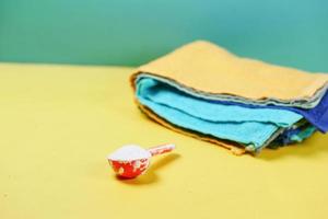 Washing powder in plastic spoon and cloths in a yellow background photo
