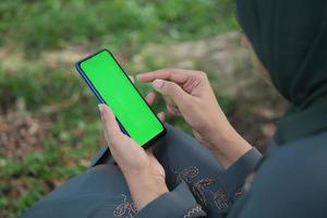 vista trasera de mujeres jóvenes usando un teléfono inteligente con pantalla verde sentada en el parque foto