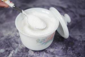 white sugar and spoon in a container on black background, photo