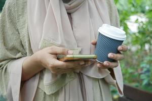 women hand holding smart phone and paper coffee cup photo